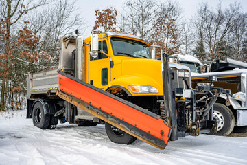 Yellow big rig semi truck tractor with snow shovel and compact dump truck body standing in row on...