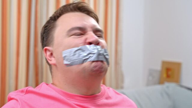 Mouth taped, freedom of speech, censorship Portrait of tied up man, mouth is covered with tape, he protests, he resists with his voice, he shouts insults, threats, Fuck you Torture, domestic violence