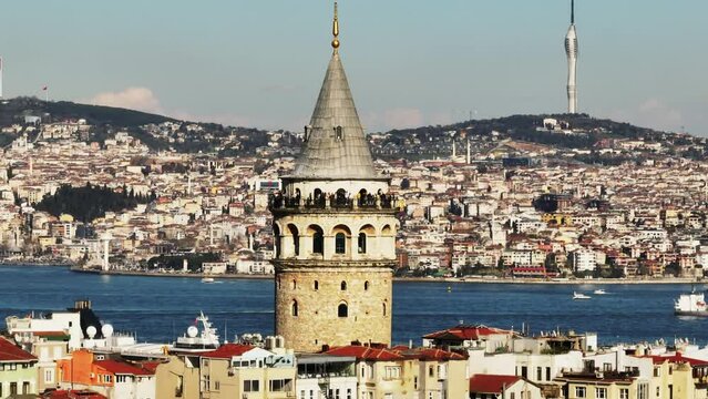 People enjoying sunny day on observation terrace of historic Galata Tower. Boats on water surface and building on opposite bank in background. Istanbul, Turkey