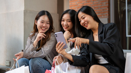 Group of fun Asian female friends are watching something fun on a phone while sitting on the stairs