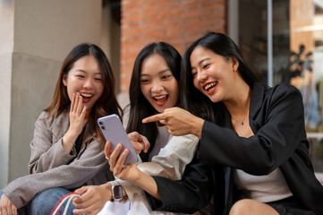 Group of fun Asian female friends are watching something fun on a phone while sitting on the stairs