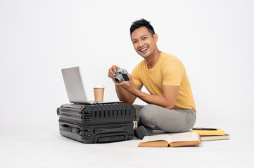 A man is preparing his luggage for his holiday trip, checking his camera, isolated background.