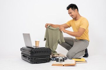A happy Asian man is excited for his holiday trip, packing his luggage, isolated white background.