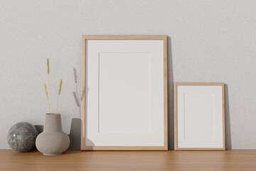 Two minimal picture frames mockup and a ceramic vase on a wooden tabletop against the white wall.