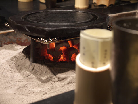 Starting japanese fine dinner with heating the iron frying pan on glowing red coals in traditional irory hearth