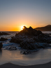 Sunlight star behind rock formation on the beach.