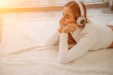 Top view portrait of relaxed woman listening to music with headphones lying on carpet at home. She...