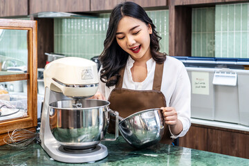 Young asian women i s shop owner Put on an apron making cream for cupcakes, Using electric mixer,...