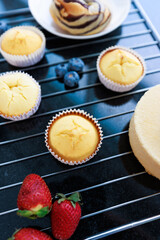 Top view closeup shot of delicious tasty homemade baking cupcakes and chiffon sponge cake placed on black grill plate with organic fresh mixed berries strawberry blackberry blueberry in kitchen