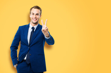 Excited businessman in confident suit showing two fingers or victory sign gesture, against yellow...