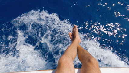 An aerial view of men's bare feet hanging from the side of a ship. Men's feet against the...