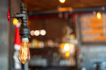 A classic design ceiling lightbulb is glowing in orange warmlight shade with blurred background of...