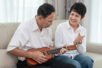 Asian okd couple sing a song and play ukulele togather in living