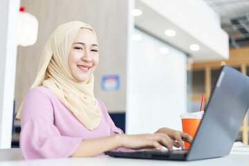 Beautiful independent Muslim woman working in a coffee shop or restaurant alone. She uses the computer to do work and search for information in the restaurant.