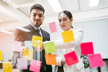Group of successful Asian businessmen teamwork. Brainstorm meeting with sticky paper notes on the glass wall for new ideas. Using agile methodology for business in a tech start-up office.