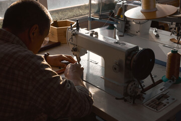 old talented man sews a leather belt in his workshop studio. back view photo. lifestyle, hobby,...