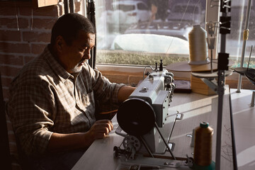 serious artisan concentrated on fixing leather belt. close up side view portrait. loft interior in...