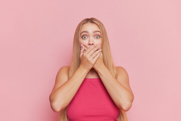 Portrait of slim girl with long gold hair wearing pink top covering her mouth over background, beautiful people concept, copy space - obrazy, fototapety, plakaty