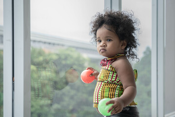 Portrait of a 2-year-old Nigerian girl with beautiful curly hair standing and looking out of the...