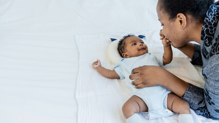 an African newborn baby is 2 months old lying on a white bed smiling happily When he is looking at his mother, to relationship in African family and black newborn concept.