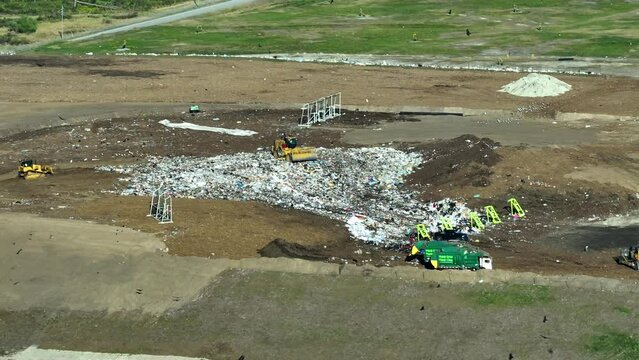 Garbage landfill site with bulldozer tractors burying large amount of trash under the ground. Harmful impact of open waste management on environment