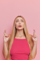 Closeup shot of pretty girl with long fair hair in pink top standing on pink background pointing...