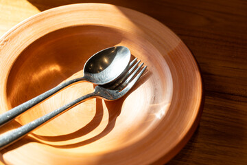 Close up stainless steel cutlery on clay plate. Clay Plate with spoon and fork on wooden table with...