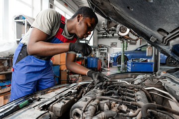 Fototapeta na wymiar Young African auto mechanic checking car engine under the hood in auto service