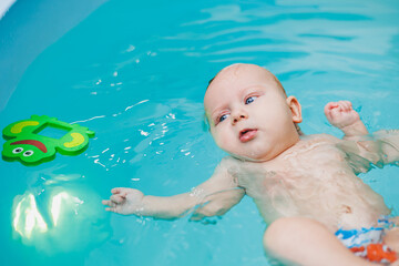 Fototapeta na wymiar Teaching children to swim. A baby learns to swim in a pool with a trainer. Baby learning to swim. Child development.