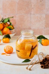Whole tangerines in syrup with cinnamon sticks and vanilla in a glass jar on a light concrete background. Sweets, preserves, preparations.