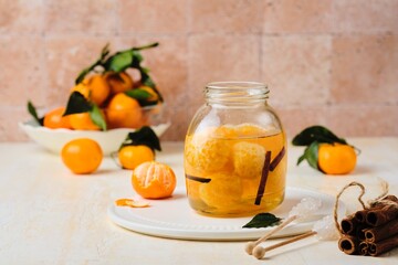 Whole tangerines in syrup with cinnamon sticks and vanilla in a glass jar on a light concrete background. Sweets, preserves, preparations.