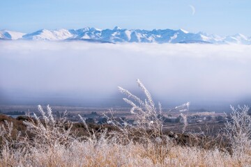 Frosty grass against snowy mountains and fog above the village. Utah. USA