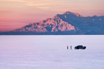 Two people with car on Salt Flats near Salt Lake City at sunset. Utah. USA