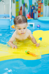 Fototapeta na wymiar Little cheerful 2-year-old boy is learning to swim in the pool. Swimming lessons for children. Swimming school for children.