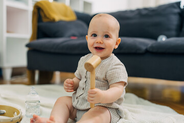Adorable Caucasian baby sitting on the floor and playing with wooden hammer.