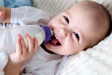 A child drinks milk from a baby bottle. Baby girl, top view, in white clothes, European appearance. Nutrition, choice of natural or artificial feeding.
