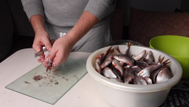 A man will gut the river fish with a knife. For drying in the oven. Next to him is a basin with fish
