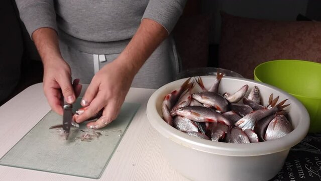 A man will gut the river fish with a knife. For drying in the oven. Next to him is a basin with fish.