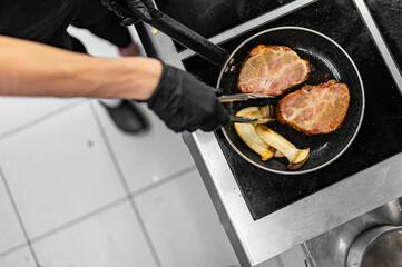 Professional chef cooking beef steak in frying pan on stove in restaurant kitchen