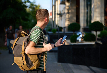 Young sporty man in a striped T-shirt walking on the street with a smartphone in hand and a trendy...