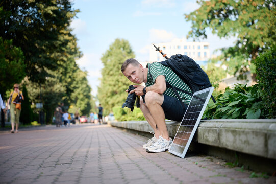 Traveling photographer using solar panel to charge his camera. Young traveler waiting for his camera to charge. Positive male relaxing after long walk.