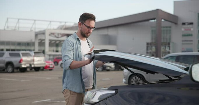 Sad Disappointed Man looking under opened car hood inspecting checking engine for overheating or liquid level