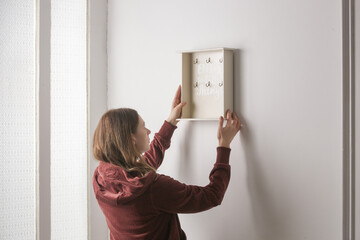 Young woman is hanging wooden key holder on the wall, moving into the new apartment or home decor...