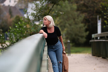 Woman in her forties, with a black shirt and jacket in her hand, rests her arm on a railing and looks to the right into the distance.