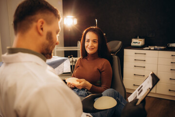 Breast implant. Dark-haired woman choosing breast implant while visiting professional plastic...