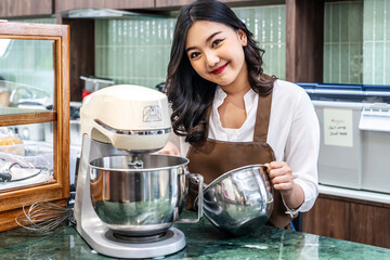 Young asian women i s shop owner Put on an apron making cream for cupcakes, Using electric mixer,...