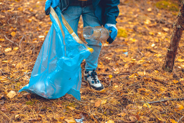 A child volunteer collects plastic waste in a garbage bag. A child eco activist saves the forest...