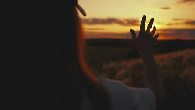 Girl looks at the sun through her hand at sunset.