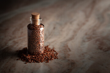 A small glass bottle filled with organic Flaxseeds (Linum usitatissimum) is placed on a marble background.