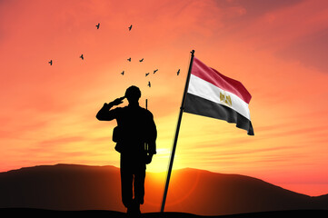 Silhouette of a soldier with the Egypt flag stands against the background of a sunset or sunrise....